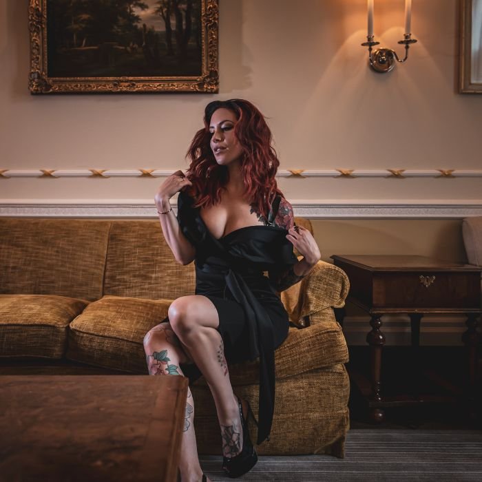 Mistress Adreena sitting on a sofa in a luxurious room.