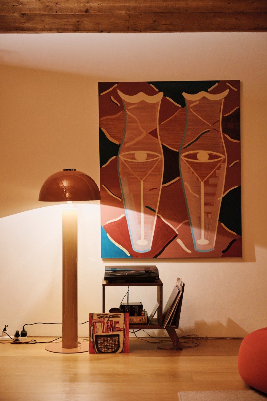 Floor lamp beside a small shelf with a record player and vinyl records under an abstract art painting.