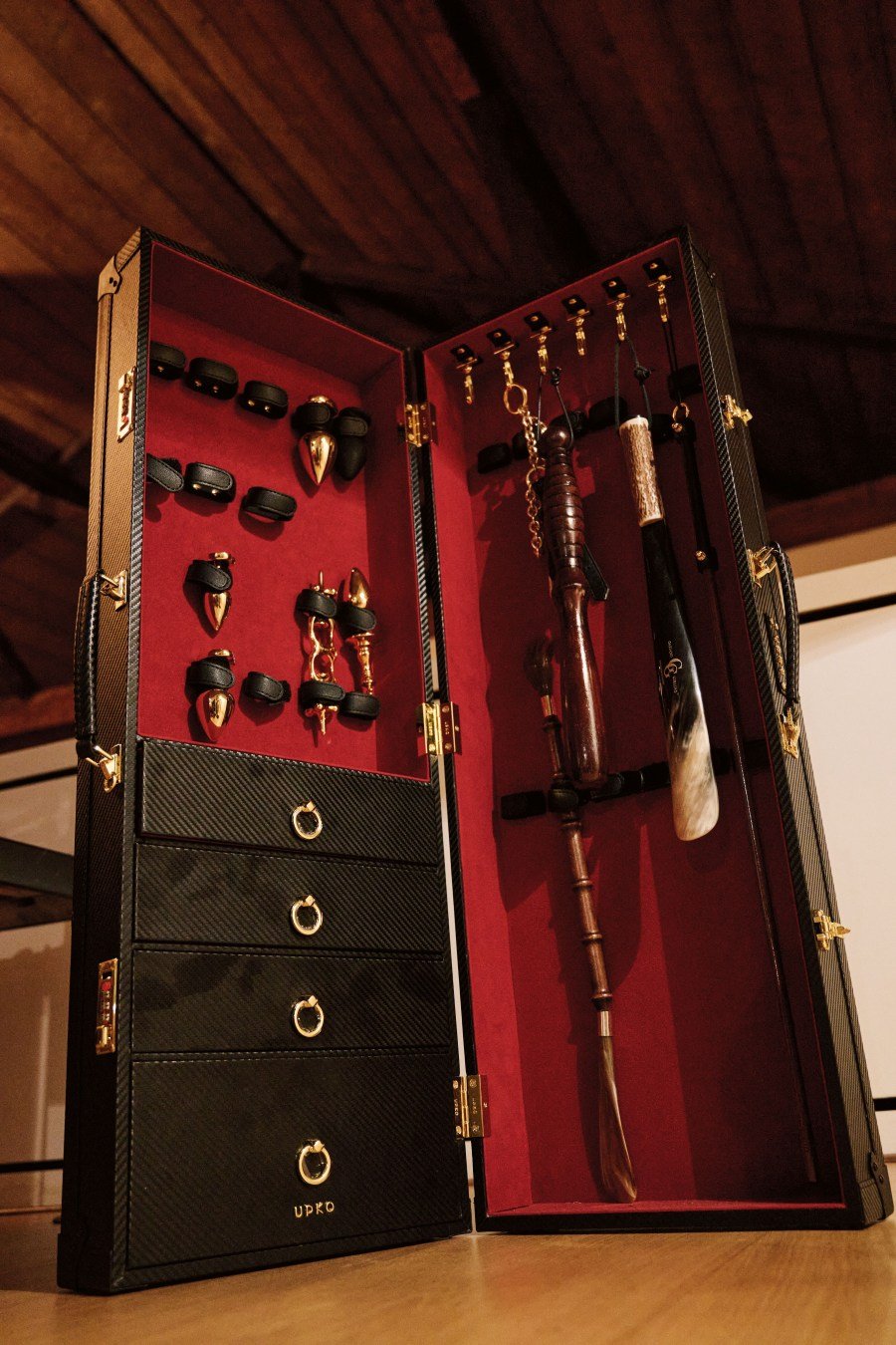 Open black case with gold hardware holding various wooden and metal walking sticks and accessories on red velvet lining.